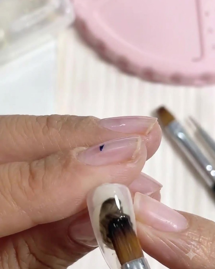 Un pinceau à ongles appliquant des touches de gel noir irrégulières sur les côtés de la plaque de longle.