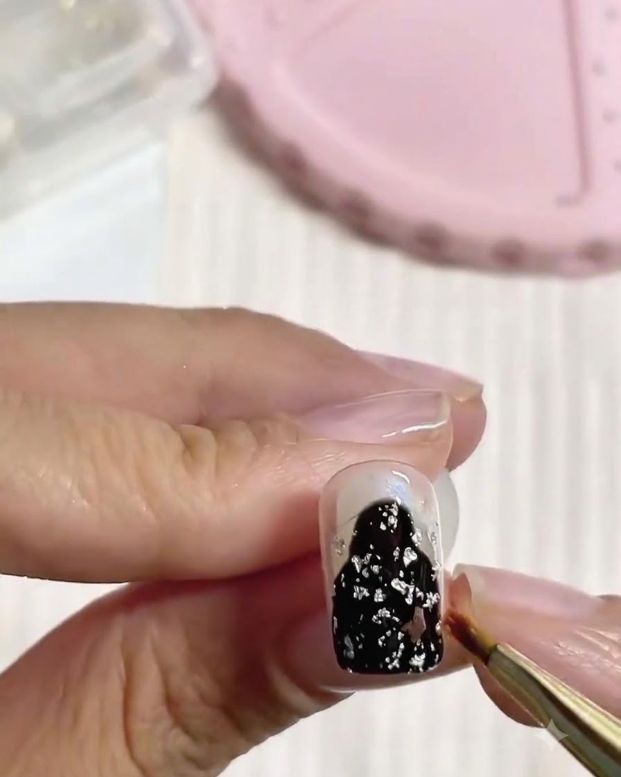 Gros plan dun doigt avec du gel noir et de la feuille dargent en cours de modelage avec un pinceau fin sous un éclairage doux.