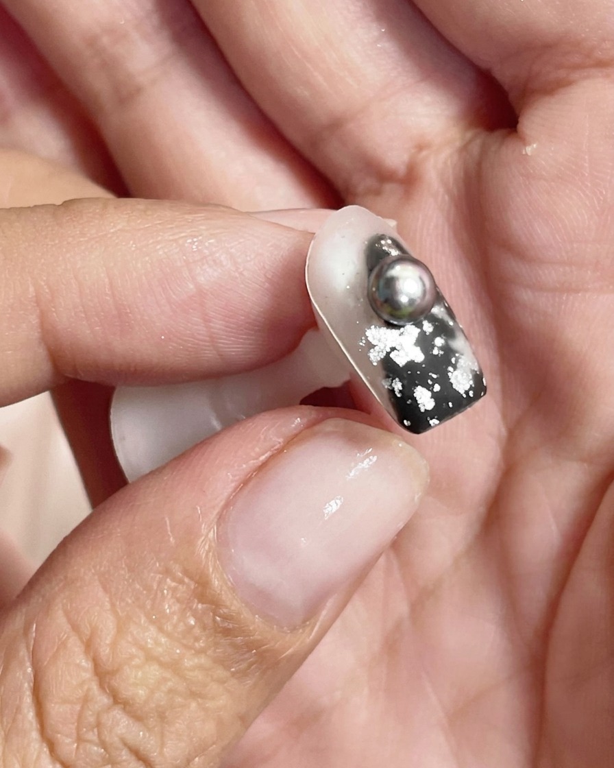Gros plan dune sphère métallique argentée brillante reflétant la lumière sur la surface dun ongle décoré.