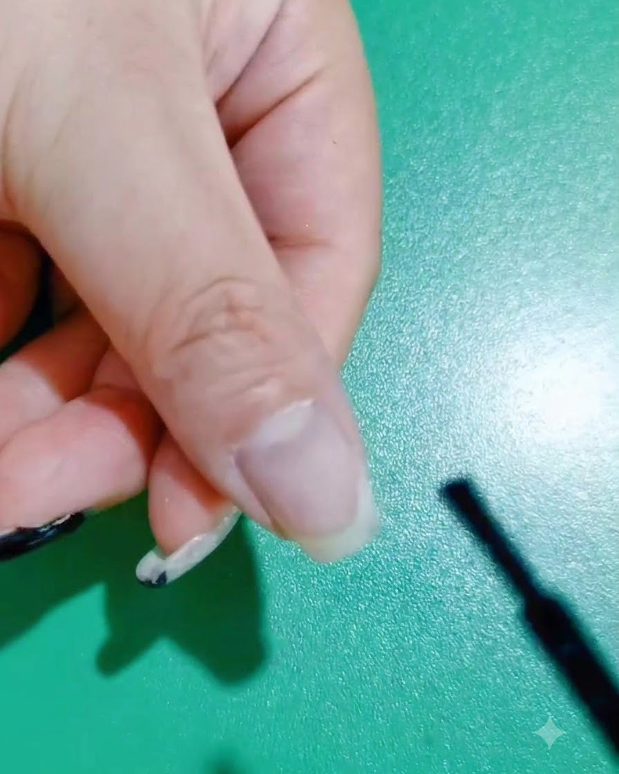Un pinceau à ongle appliquant une première couche de vernis gel noir sur un ongle naturel.