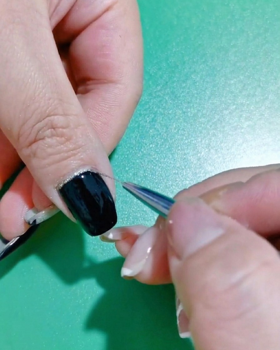 Gros plan sur un pinceau liner affinant le vernis pailleté le long du bord dun ongle noir.