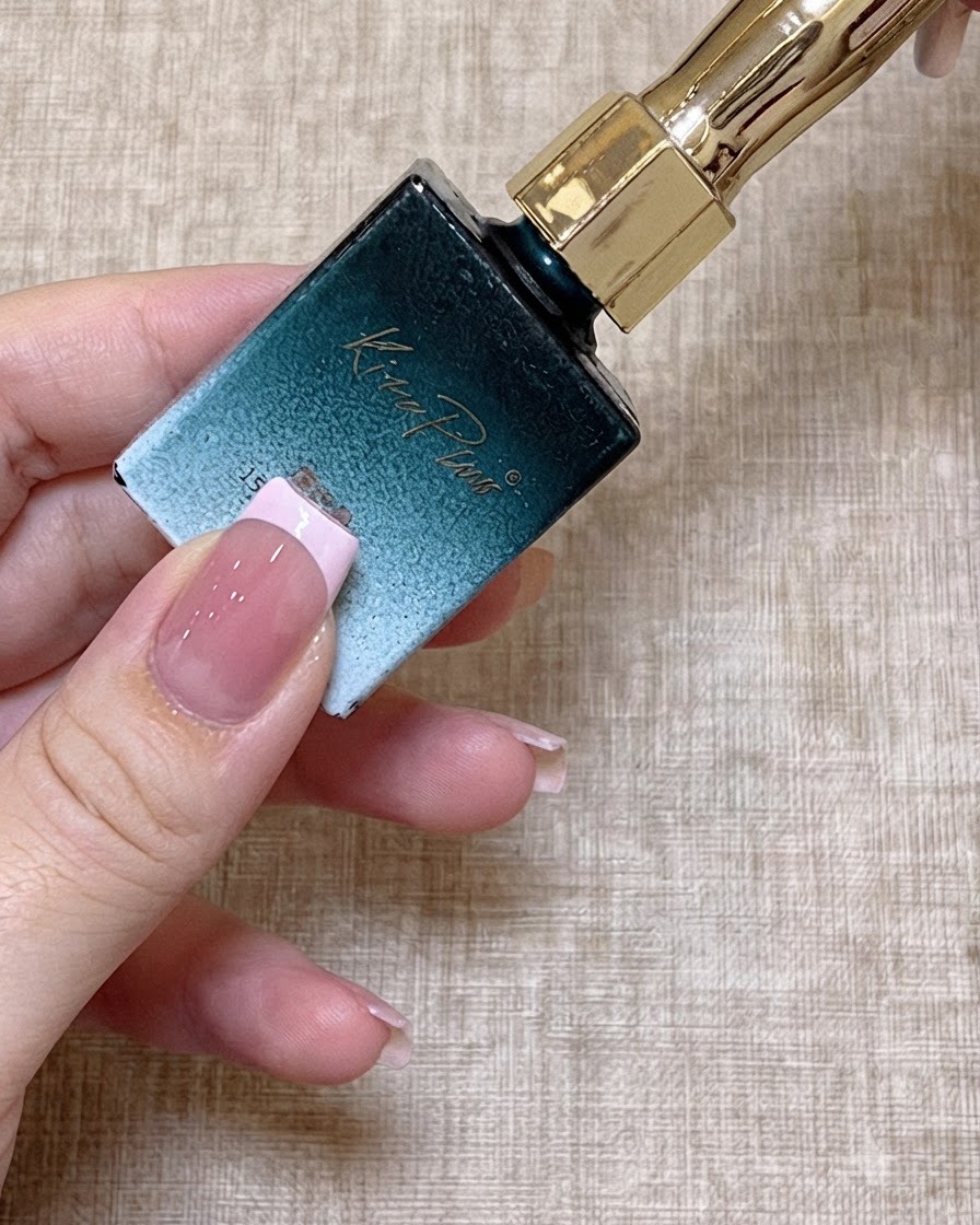 Gros plan sur un pinceau fin trempant dans un flacon de vernis gel couleur bois de rose.