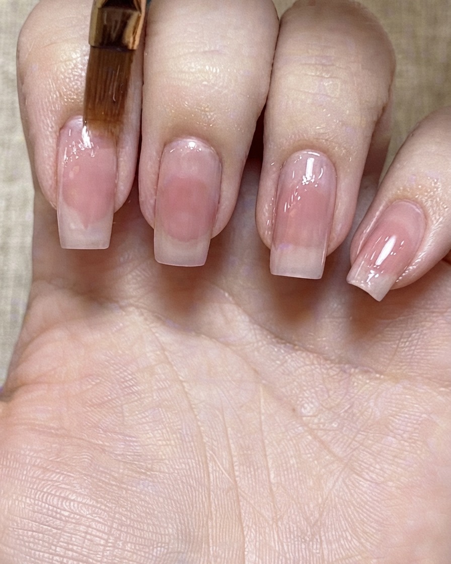 Un pinceau souple et duveteux estompant les contours dun point de gel rose sur un ongle.