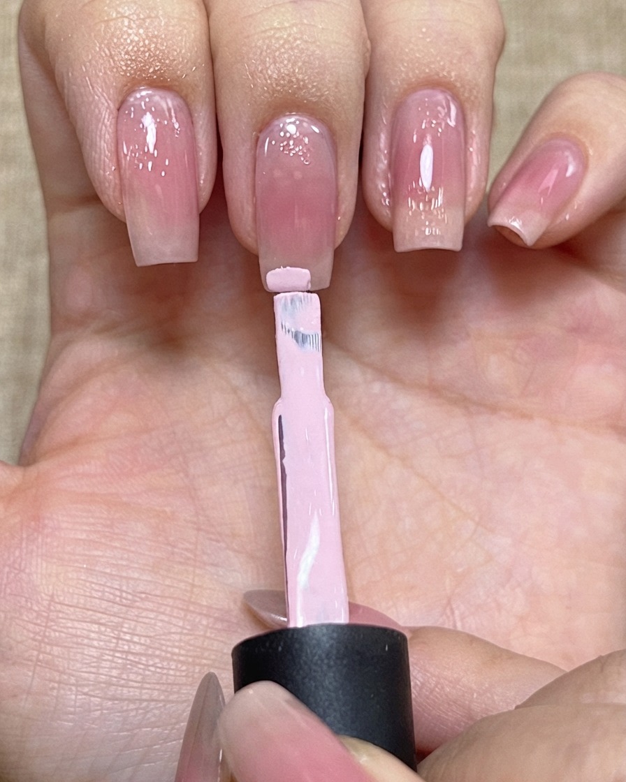 Un pinceau de vernis chargé de gel rose clair positionné près du bord dun ongle.