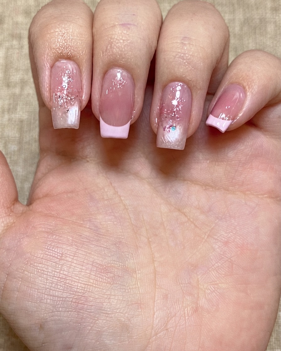Une main présentant plusieurs ongles manucurés ornés de sequins pailletés colorés éparpillés.