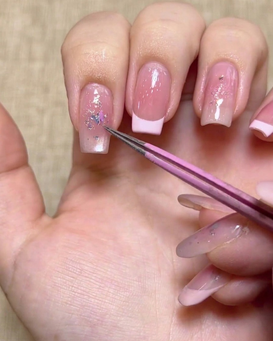 Une paire de pinces roses posant un sequin papillon irisé sur un ongle décoré.