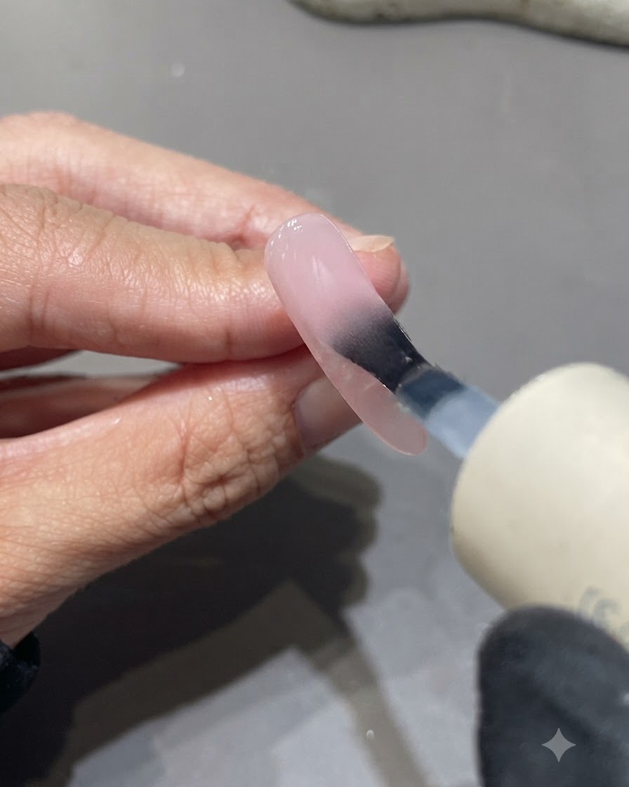 Un pinceau appliquant un top coat mat sur une surface dongle aux tons roses.