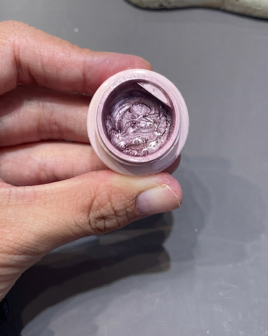 Une main tenant un pot ouvert de gel œil-de-chat argent-violet avec un pinceau liner fin trempé dedans.