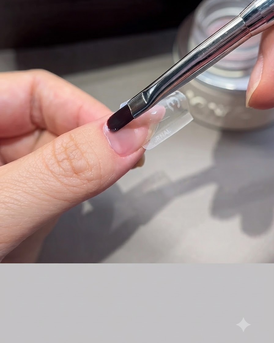Un pinceau à ongles professionnel lissant du gel dextension sur un moule transparent positionné sur un doigt.