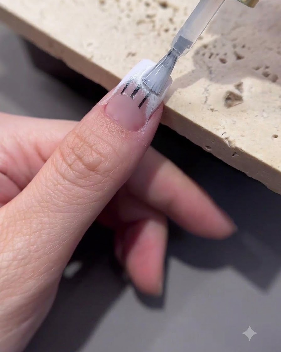 Un pinceau appliquant du gel de transfert sur la zone de la pointe dun ongle décoré.