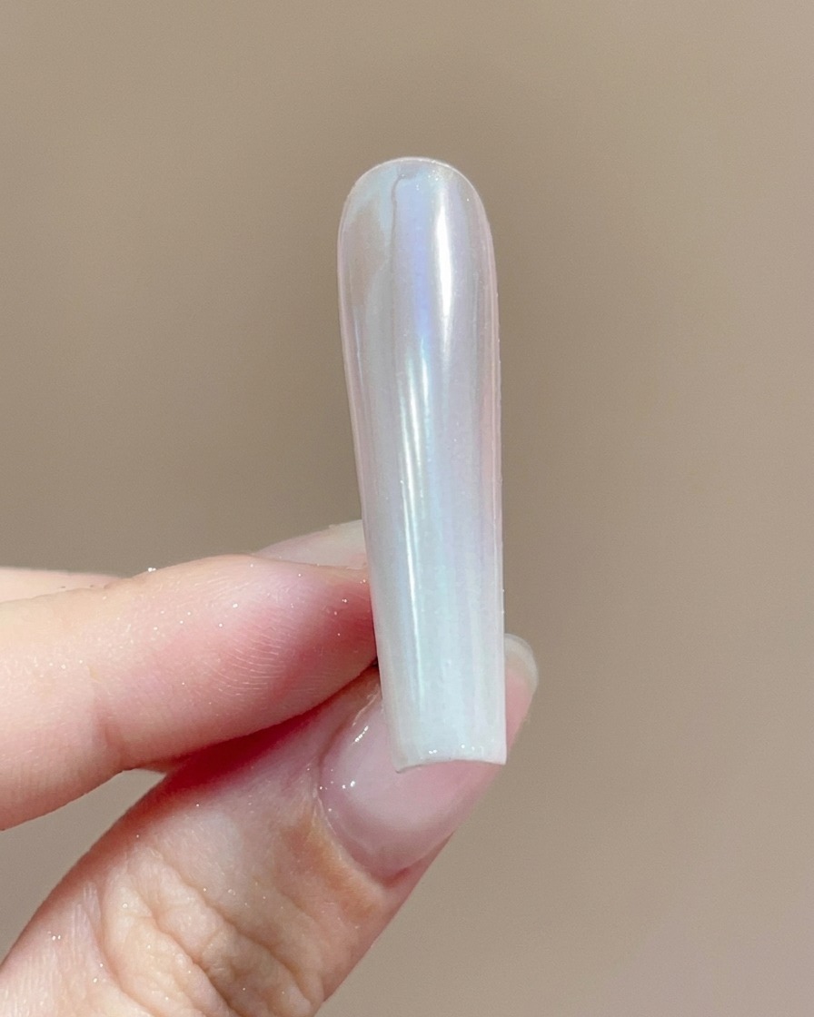 Un pinceau appliquant une couche de finition transparente sur un ongle enduit de poudre chrome chatoyante.