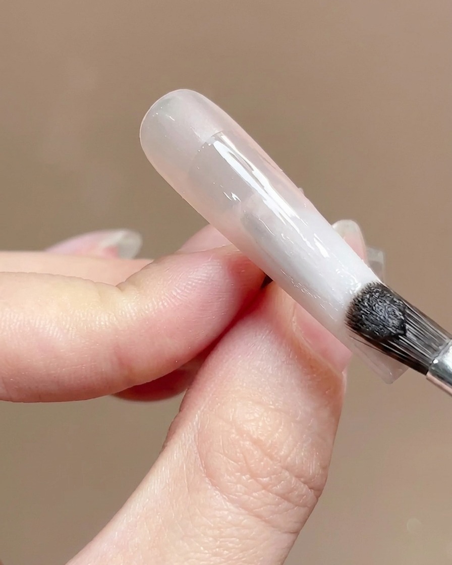 Un pinceau à ongles appliquant une couche de finition transparente et brillante sur la surface dun ongle en dégradé.