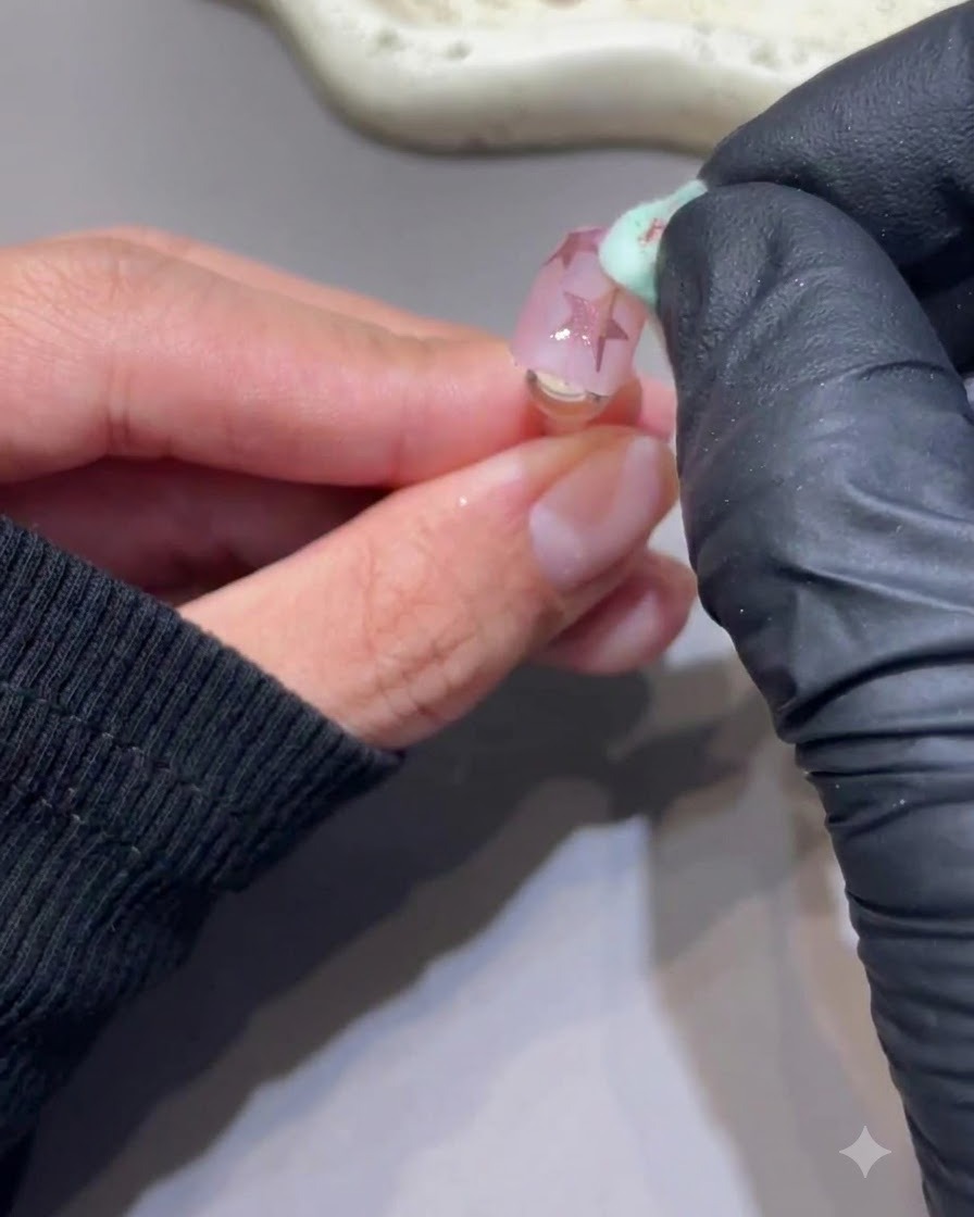 Une éponge propre brossant délicatement lexcès de poudre dun ongle comportant des étoiles en chrome rose.