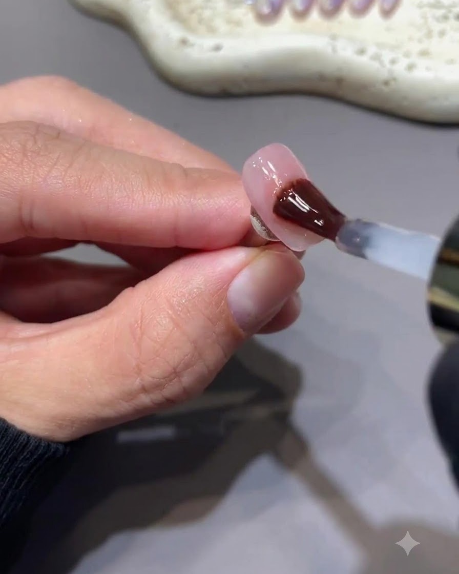 Un pinceau appliquant un top coat en gel brillant sans résidu sur un ongle avec un nail art détoiles rose baie.