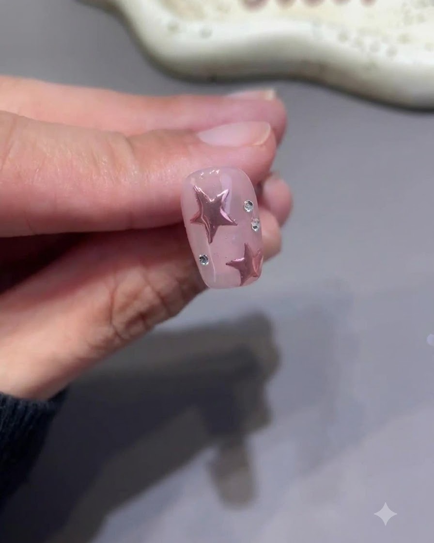 Un minuscule pinceau de détail peignant méticuleusement du top coat autour de la base de petits strass sur un ongle étoile rose fini.