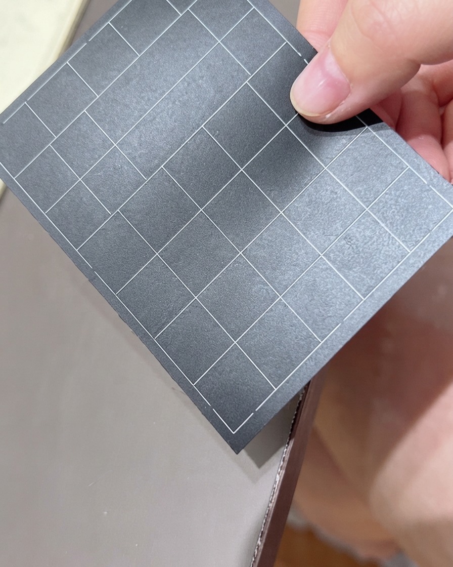 Une main tenant une feuille noire dautocollants pour ongles quadrillés, sélectionnant un autocollant.