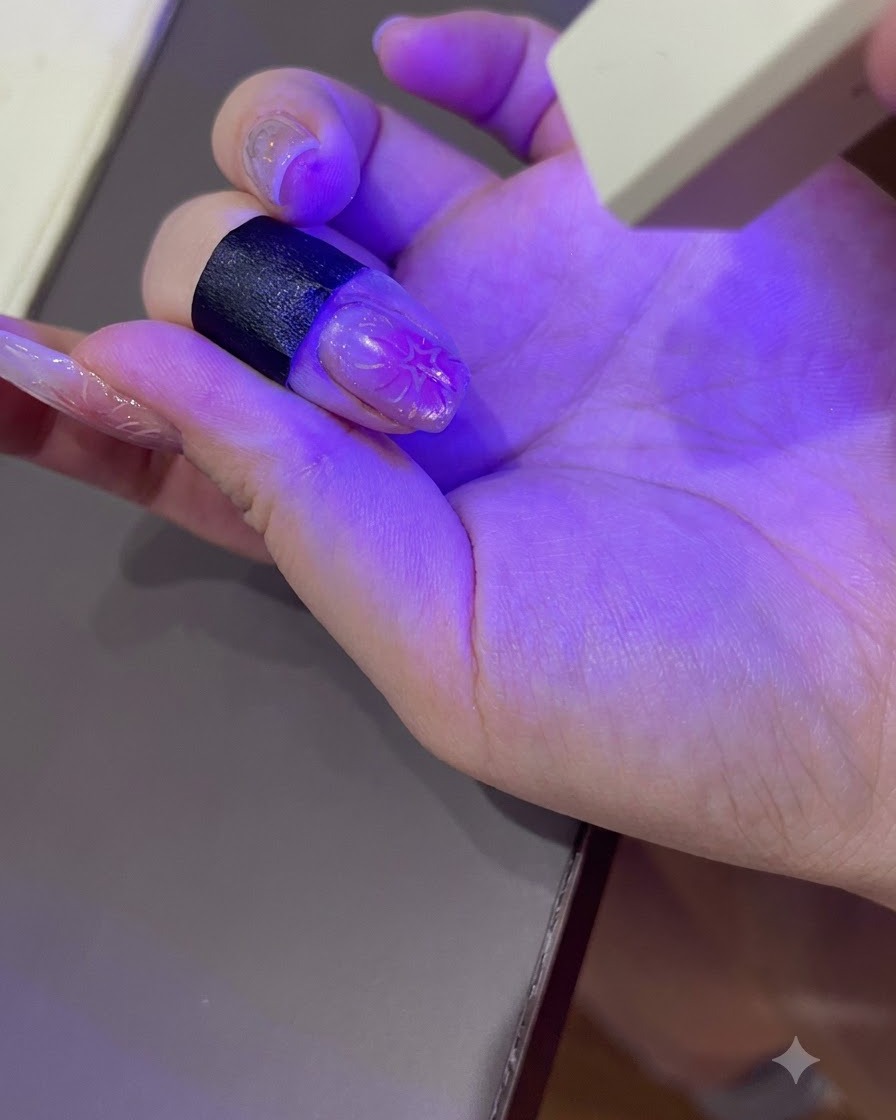 Une main manucurée catalysant sous la lumière violette dune lampe à ongles UV/LED portable.