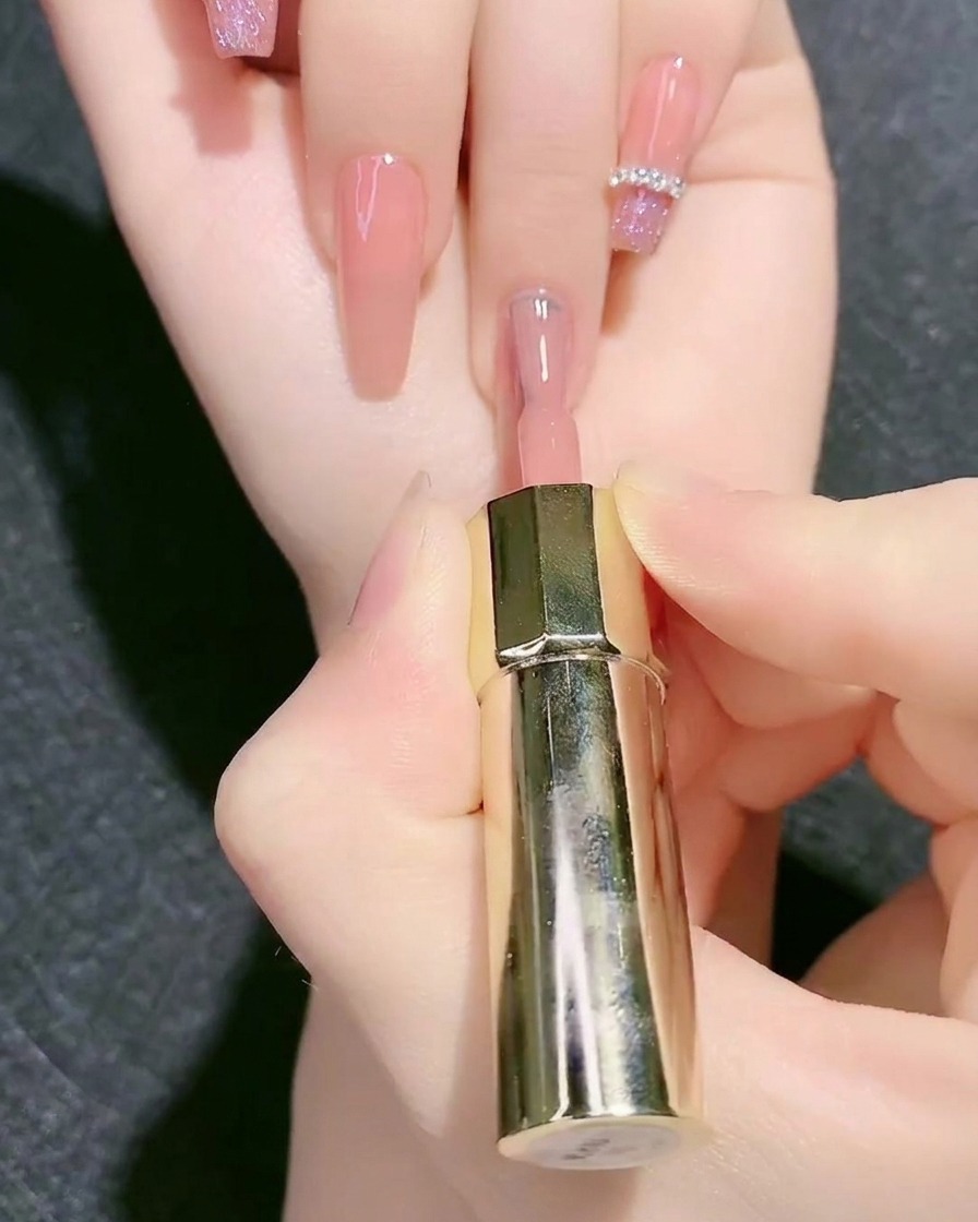 Un pinceau à vernis appliquant une couleur de base en gel rose nude sur un ongle.