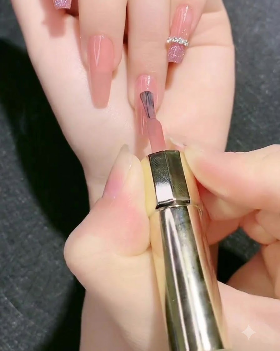 Un pinceau appliquant une seconde couche de gel de base rose nude sur longle.