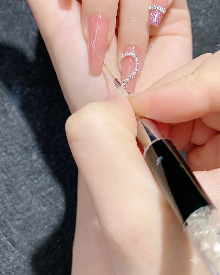 Gros plan sur une séance de nail art détaillée utilisant un outil fin pour presser des bandes de chaînes de strass sur un ongle en dégradé.