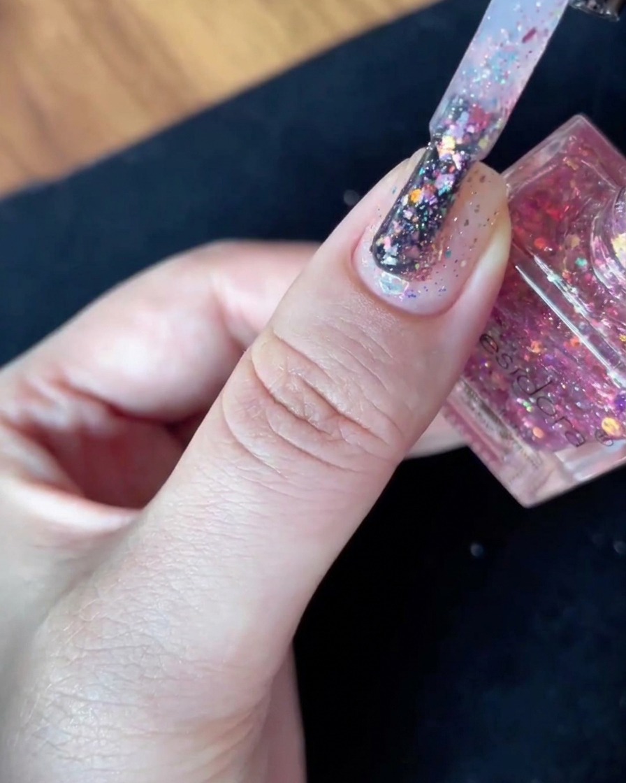 Un pinceau à vernis rempli de paillettes maintenu fermement juste au-dessus de la surface dun ongle à base nude.