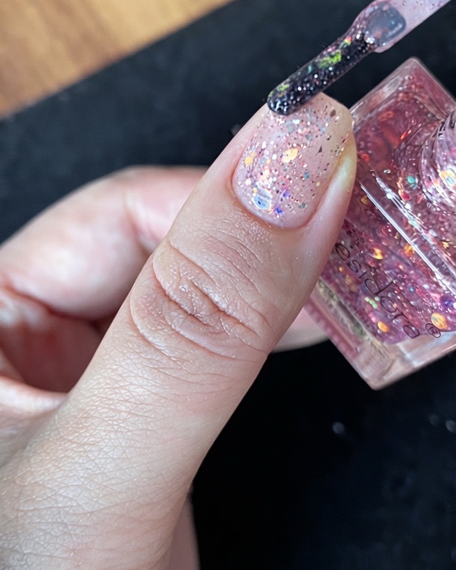 Un groupe généreux de paillettes multicolores placé directement au centre dun ongle nude.