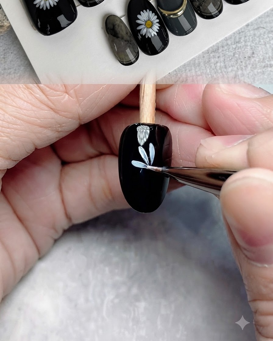 Un pinceau fin de détail ajoutant des pétales blancs supplémentaires pour achever la première couche florale sur un ongle noir.