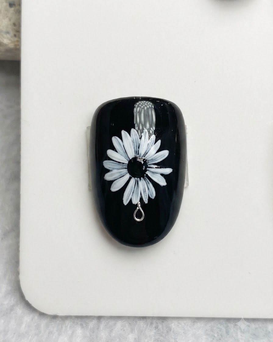 Gros plan dun pinceau à ongles appliquant de délicats points blancs et jaunes sur le centre noir dun design de marguerite blanche.