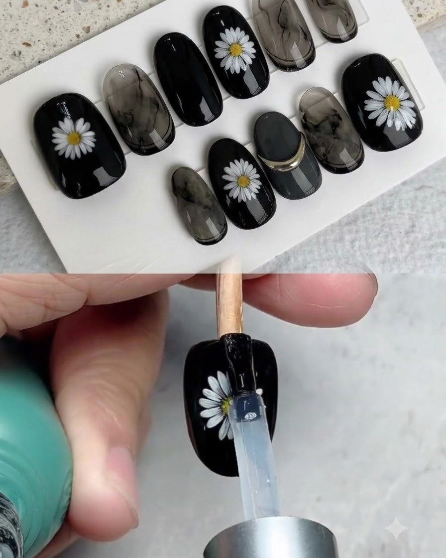 Un pinceau appliquant un top coat brillant sur un faux ongle noir fini et décoré dune marguerite blanche.