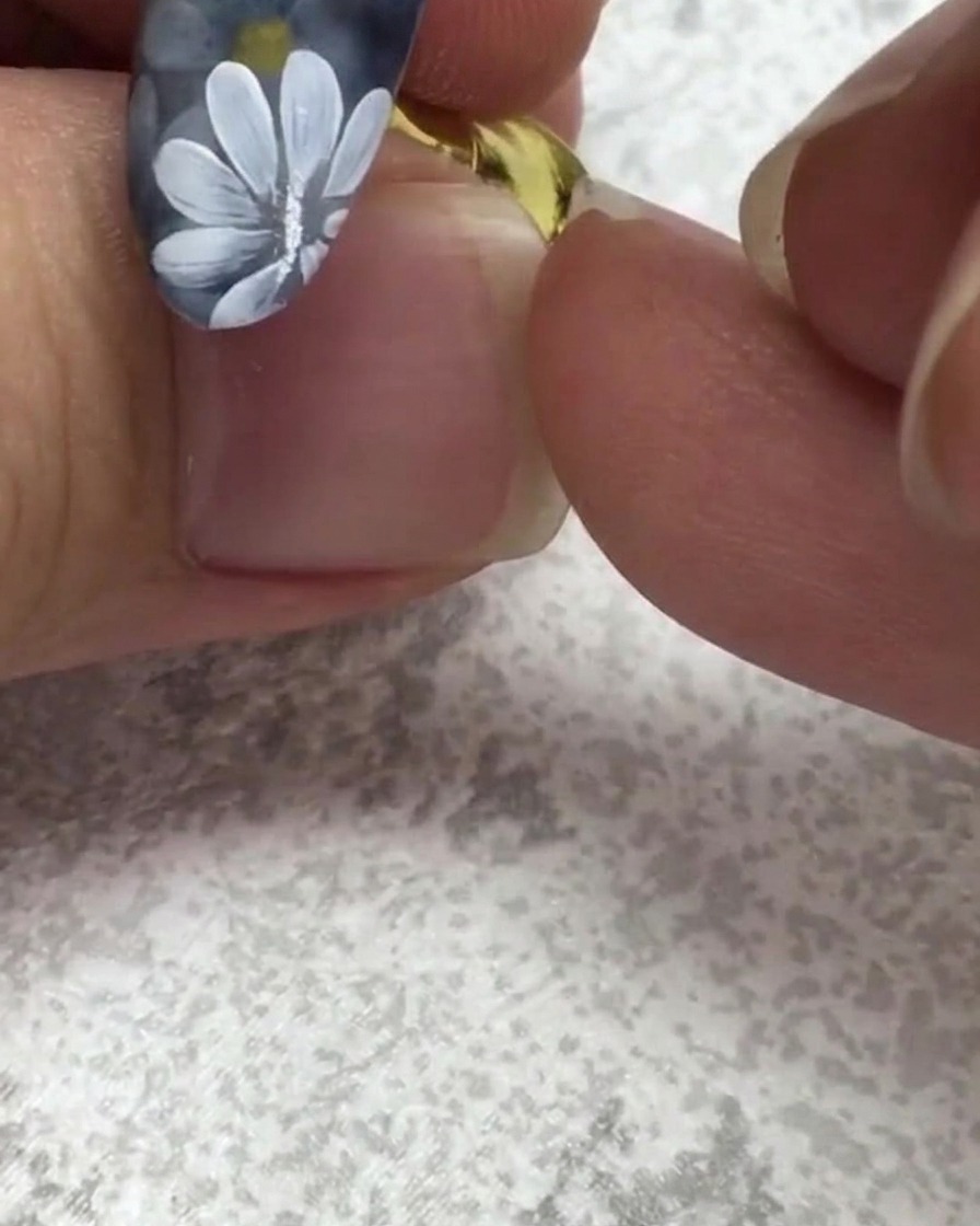 Un pinceau plat pour ongles prélevant un petit point de gel vert près dun ongle comportant des marguerites blanches.