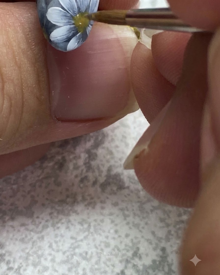 Un pinceau fin ajoutant des textures détaillées et des points à lintérieur du centre jaune dune marguerite peinte sur un ongle gris.