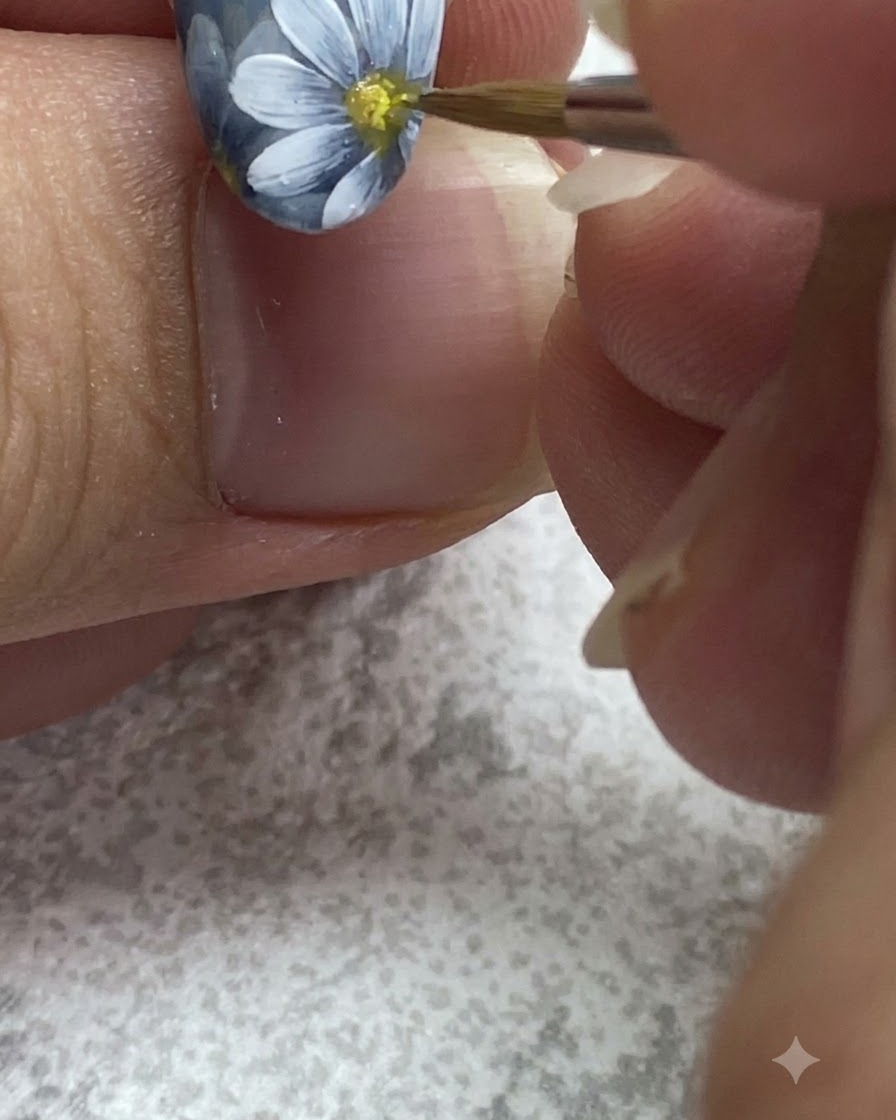 Un pinceau fin tamponnant du gel jaune au centre dune marguerite blanche peinte.