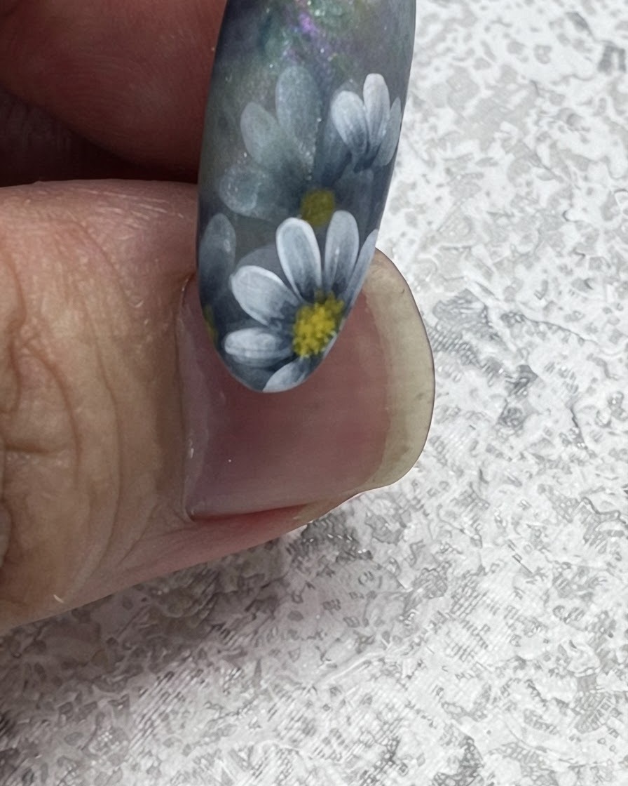 Gros plan dun pinceau à ongles tirant vers lextérieur pour créer une pointe de feuille nette à côté de marguerites peintes de style nordique.