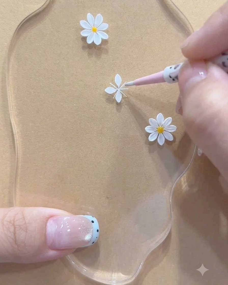 Gros plan sur un outil rose ajustant des structures de pétales peintes en blanc pour une petite marguerite sur une palette acrylique.