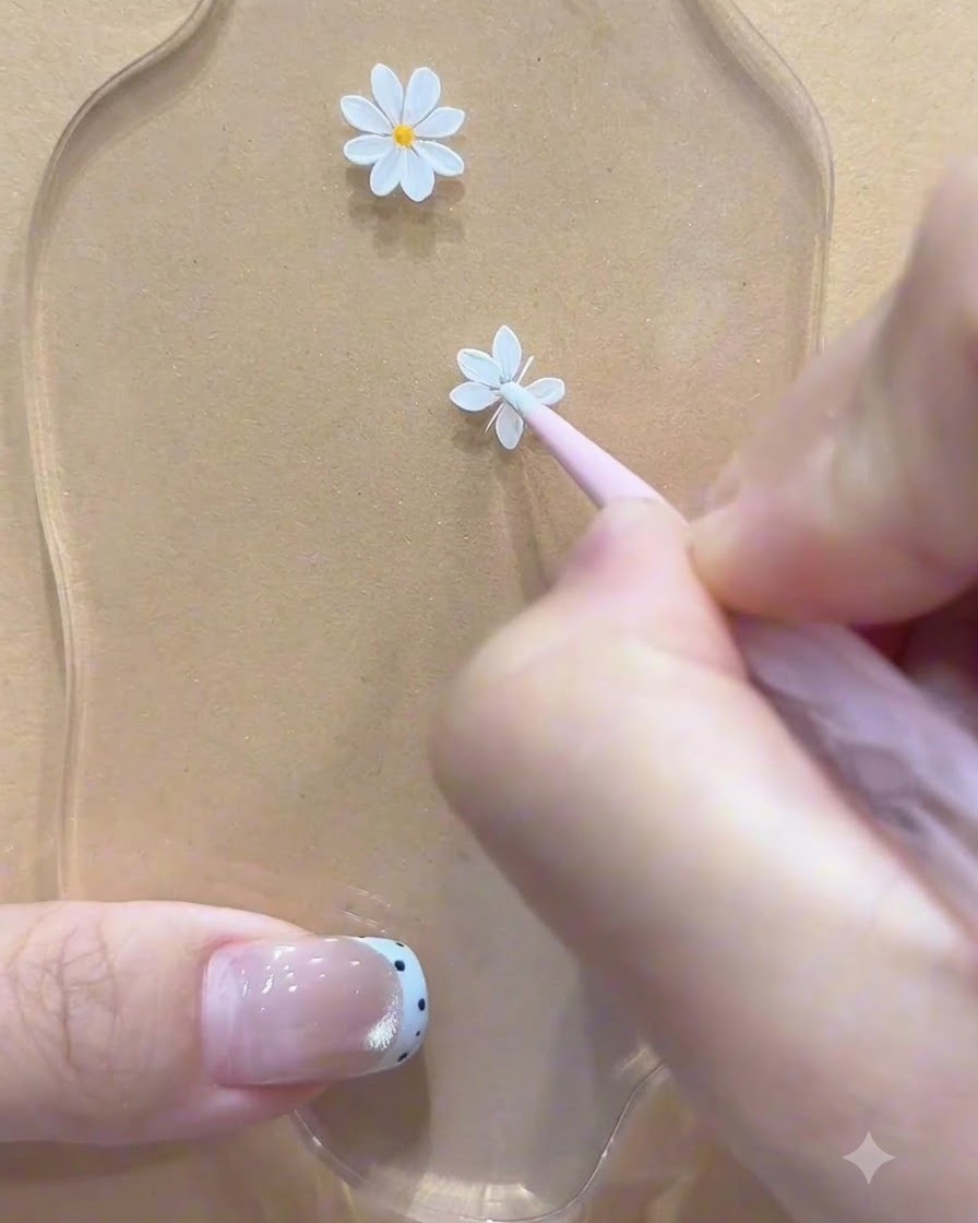 Un outil de dotting appliquant un point central jaune sur la première marguerite blanche peinte sur une surface de palette.