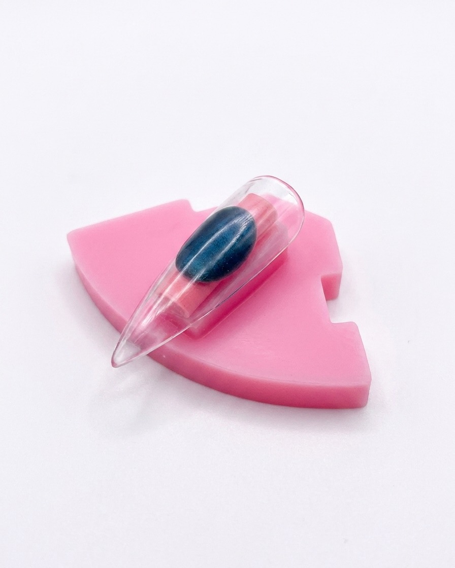 Une capsule dongle unique dotée dune finition aurora chrome affichée à la verticale sur un support rose.