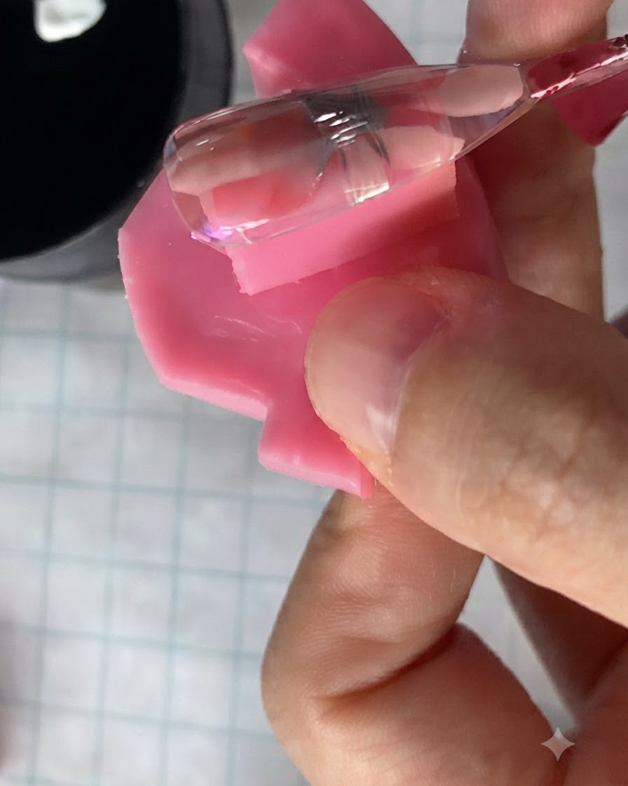Un petit pinceau à ongle appliquant un gel rose translucide sur un design de fleur de marguerite catalysé sur un ongle.
