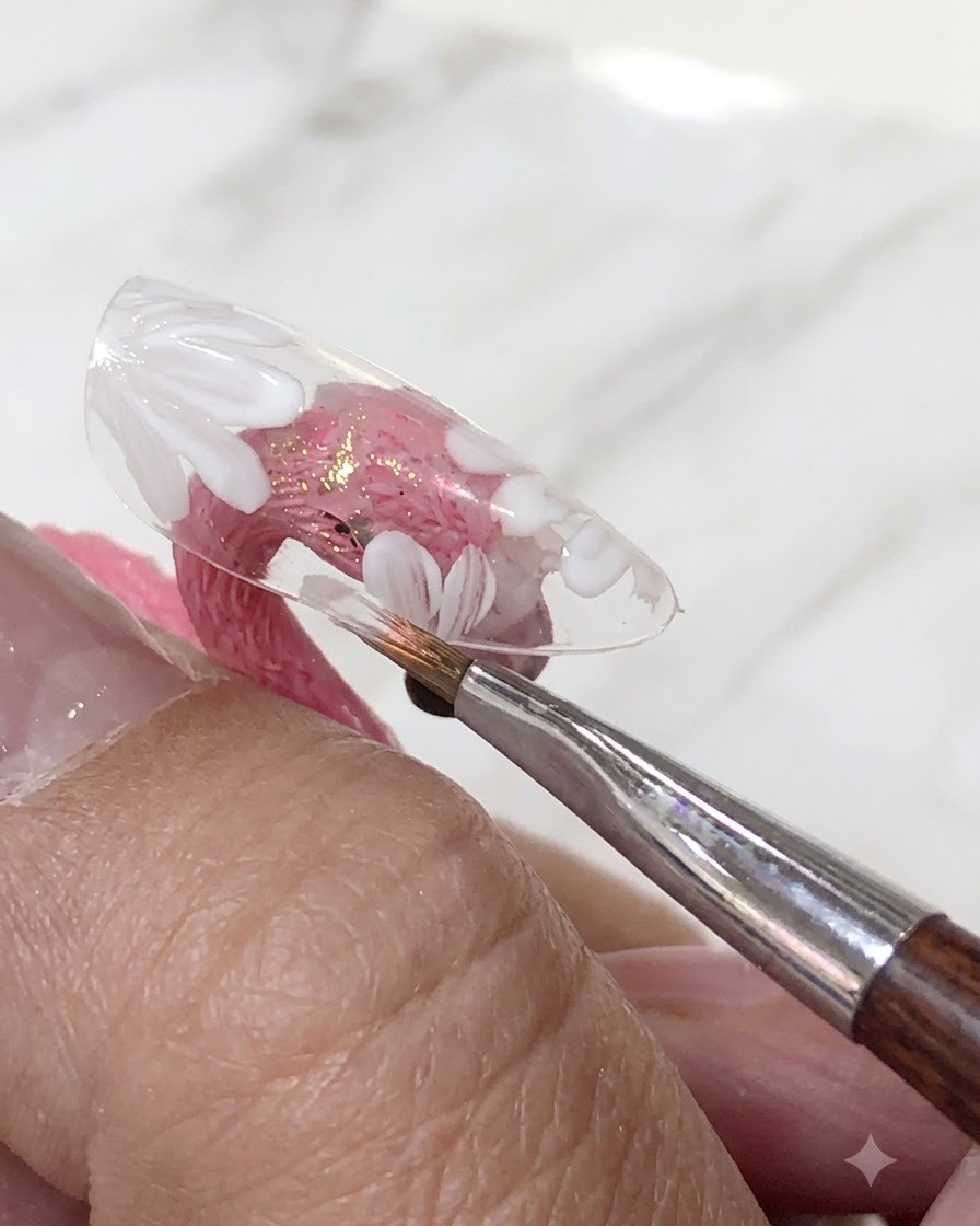 Un pinceau appliquant une couche de vernis gel rose translucide sur les fleurs blanches peintes sur une capsule dongle transparente.