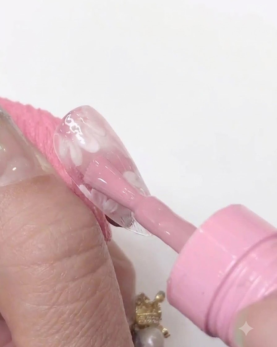 Une mini lampe à ongles UV/LED tenue de près au-dessus dune capsule transparente pour catalyser la couche de gel rose appliquée.
