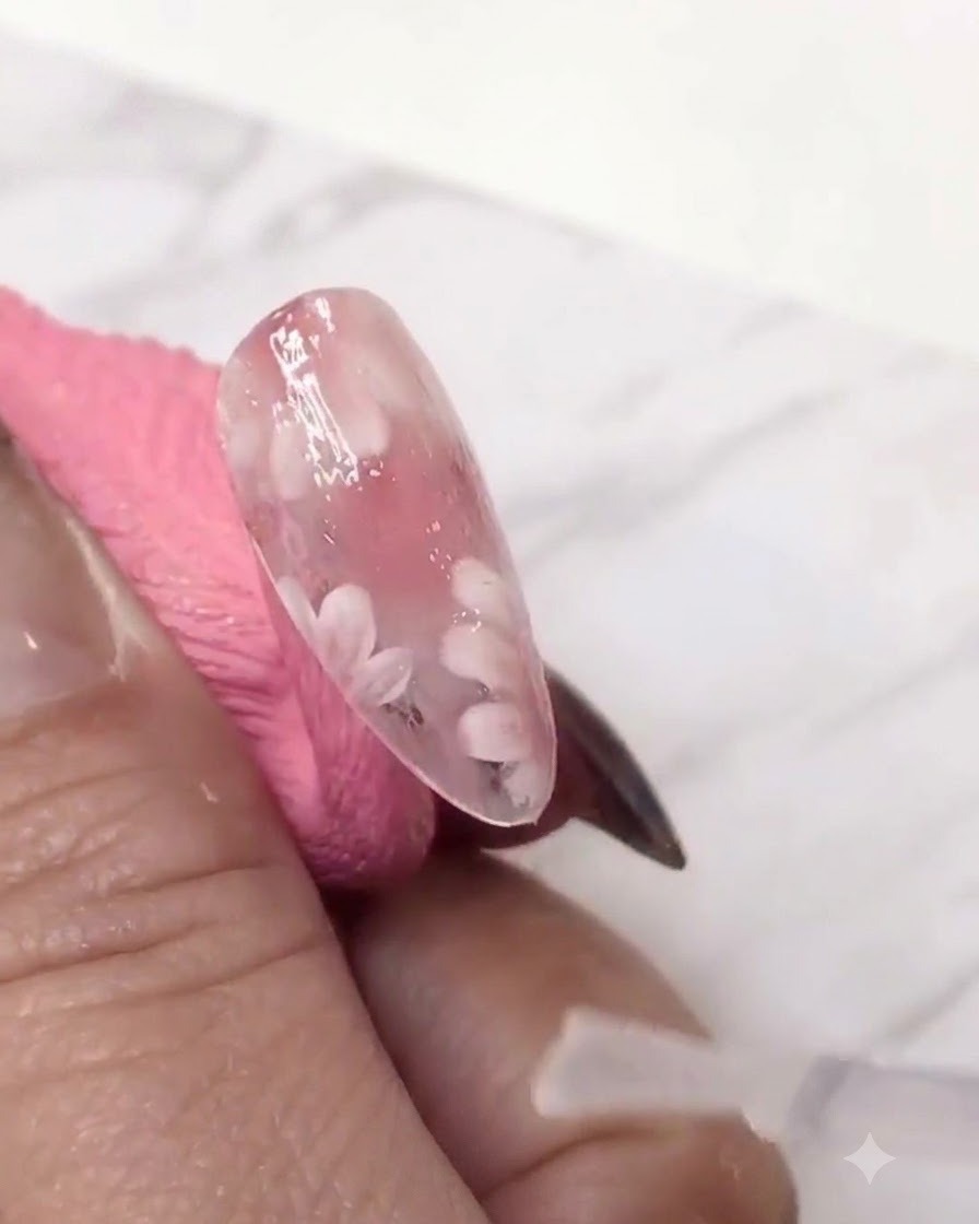Un pinceau fin ajoutant une deuxième couche de pétales de marguerites blancs sur la couche de gel teinté de rose pour plus de profondeur.