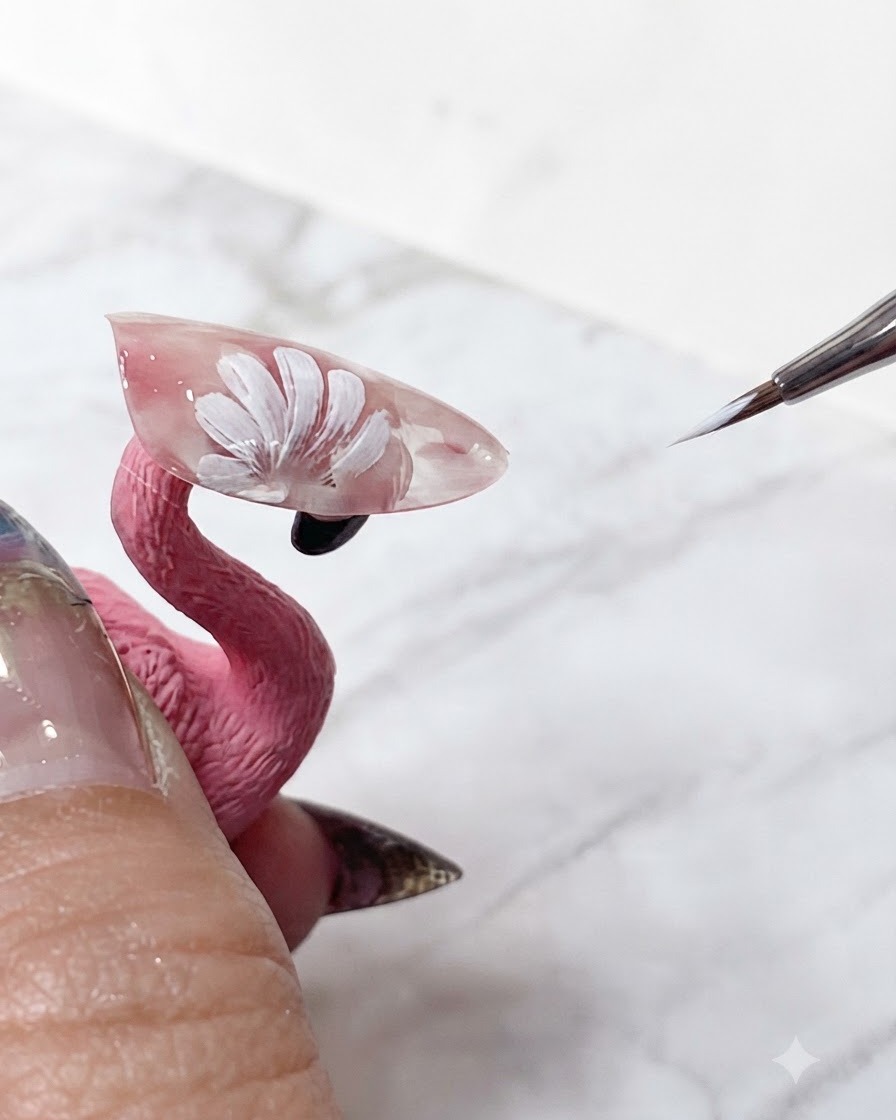 Un pinceau de nail art fin retouchant les pointes blanches nettes des pétales de marguerites superposés sur une extension rose translucide.