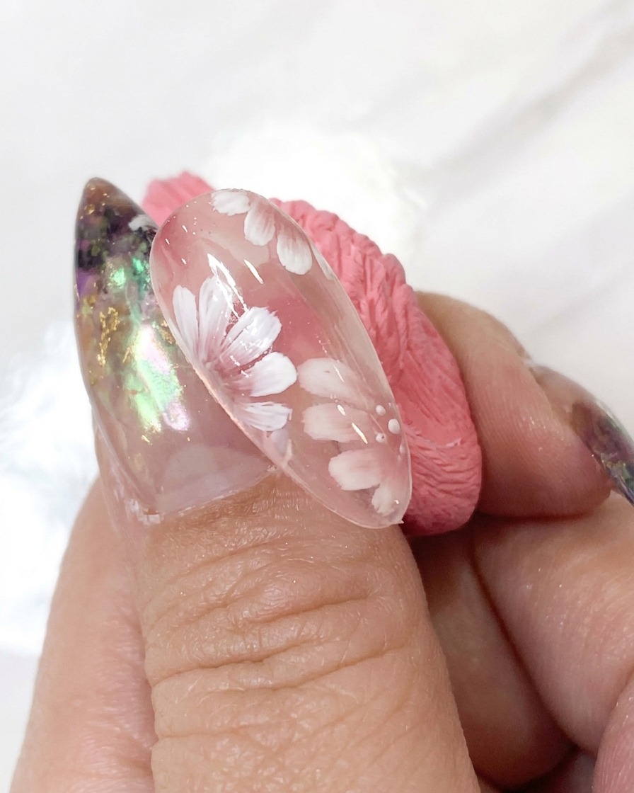 Un outil de dotting appliquant de minuscules points daccentuation blancs autour du centre de la fleur dun design de nail art détaillé.