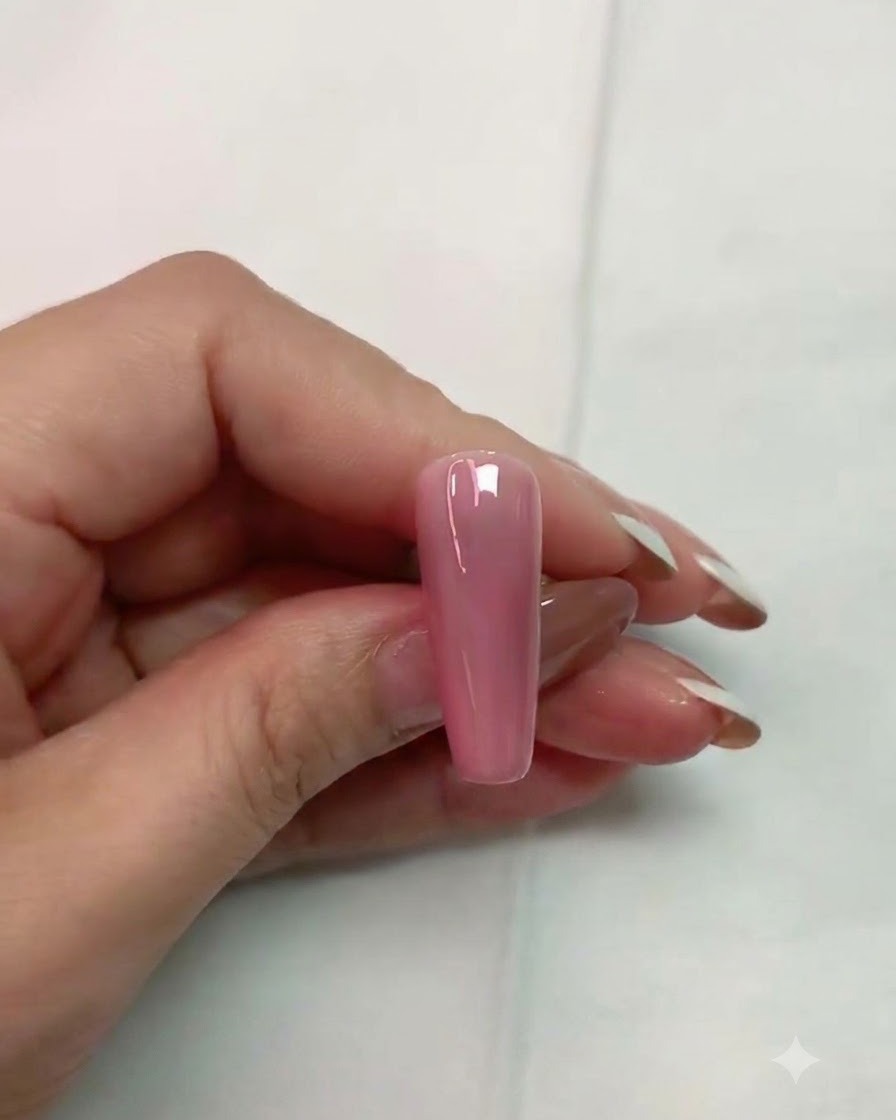 Un pinceau appliquant un top coat mat transparent sur la surface dun faux ongle rose brillant.