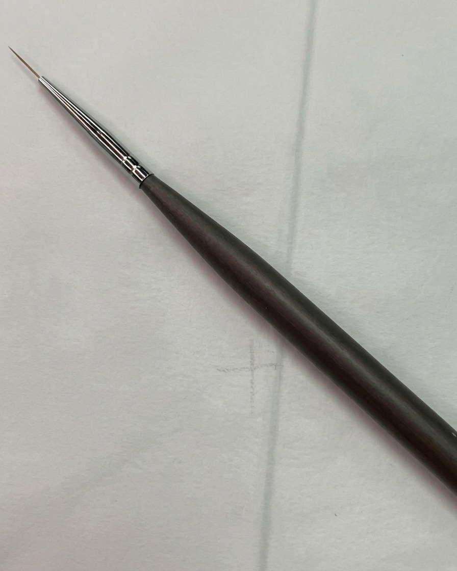 Un pinceau fin pour nail art positionné près dun croquis de grille de guidage claire sur une surface dongle dentraînement.