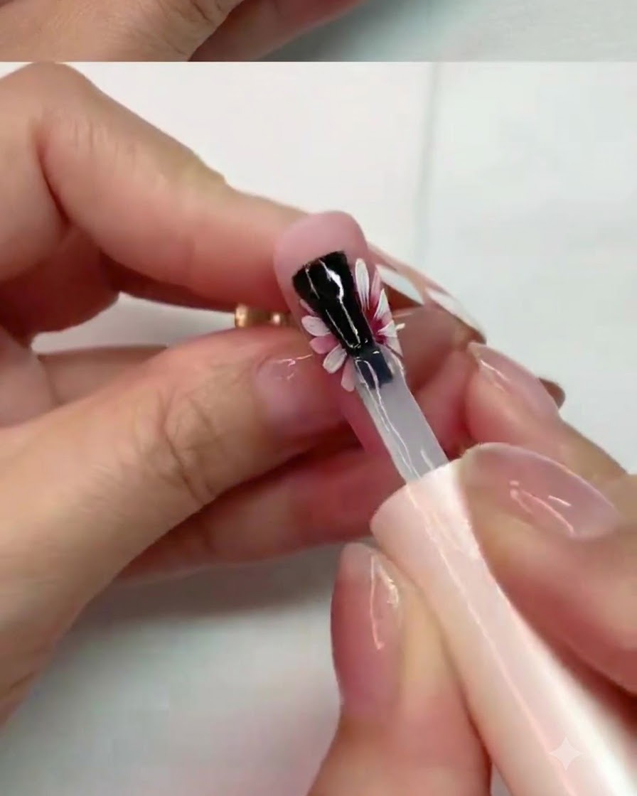 Un pinceau appliquant soigneusement un top coat mat sur les pétales du milieu dun design dongle de marguerite peint.