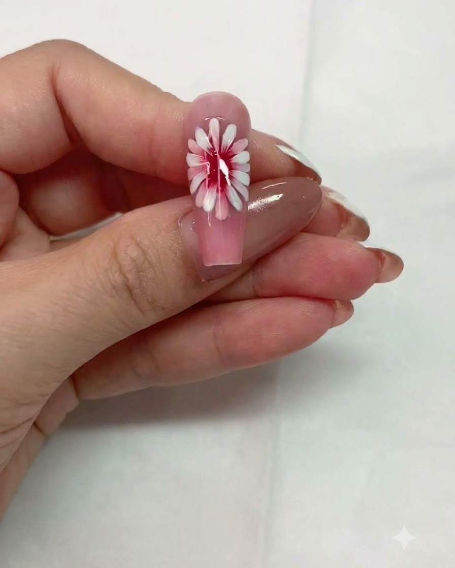 Vue rapprochée dun ongle rose avec un design de marguerite multicouche reposant avant la catalysation.