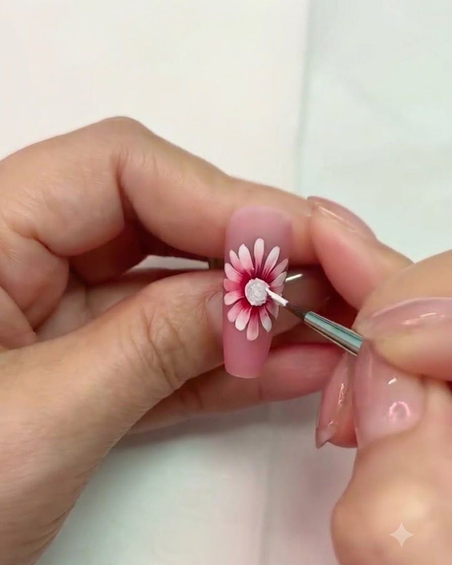 Un pinceau fin travaillant près du centre texturé blanc catalysé du nail art marguerite.