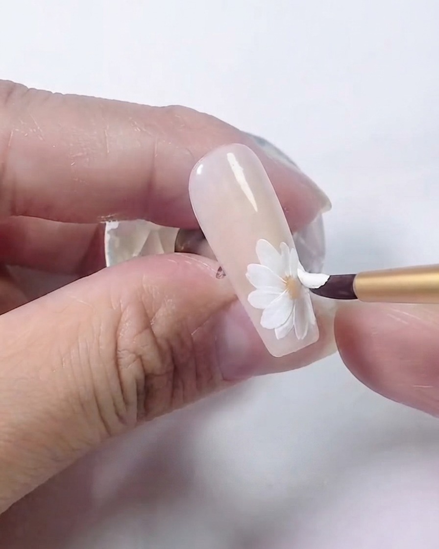 Un pinceau à ongles ajoutant une deuxième couche superposée de pétales blancs sur la marguerite.