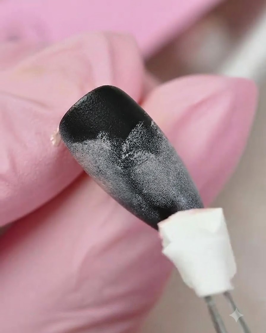 Un applicateur éponge tamponnant du gel jaune sur la partie inférieure dun ongle texturé à dégradé noir et rose.