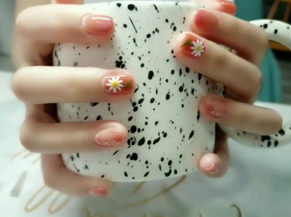 Gros plan se focalisant sur un ongle daccentuation arborant une marguerite blanche peinte à la main avec un cœur jaune et une feuille verte.